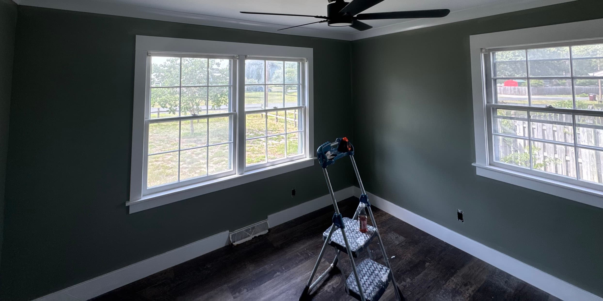 The same bedroom finished in deep green with white trim, new windows trimmed out and dark plank flooring