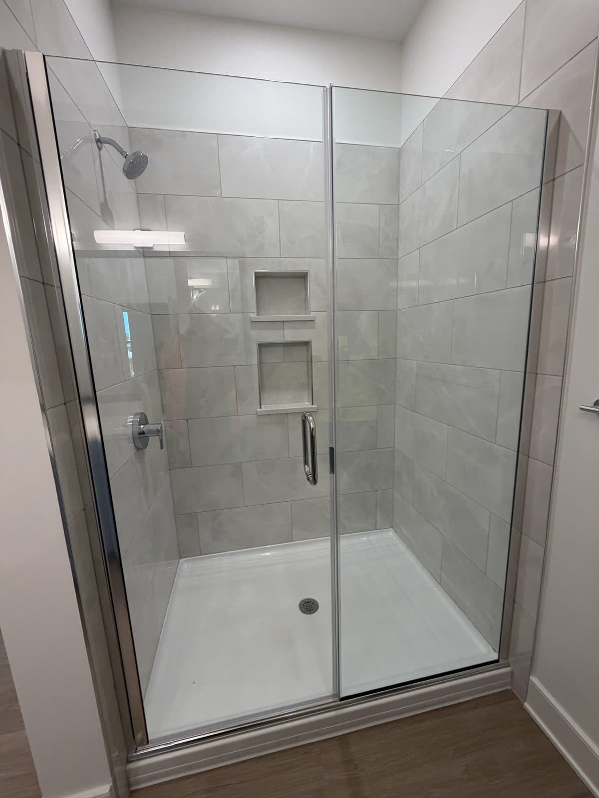 Finished large-format tile shower with twin recessed niches and a framed glass door