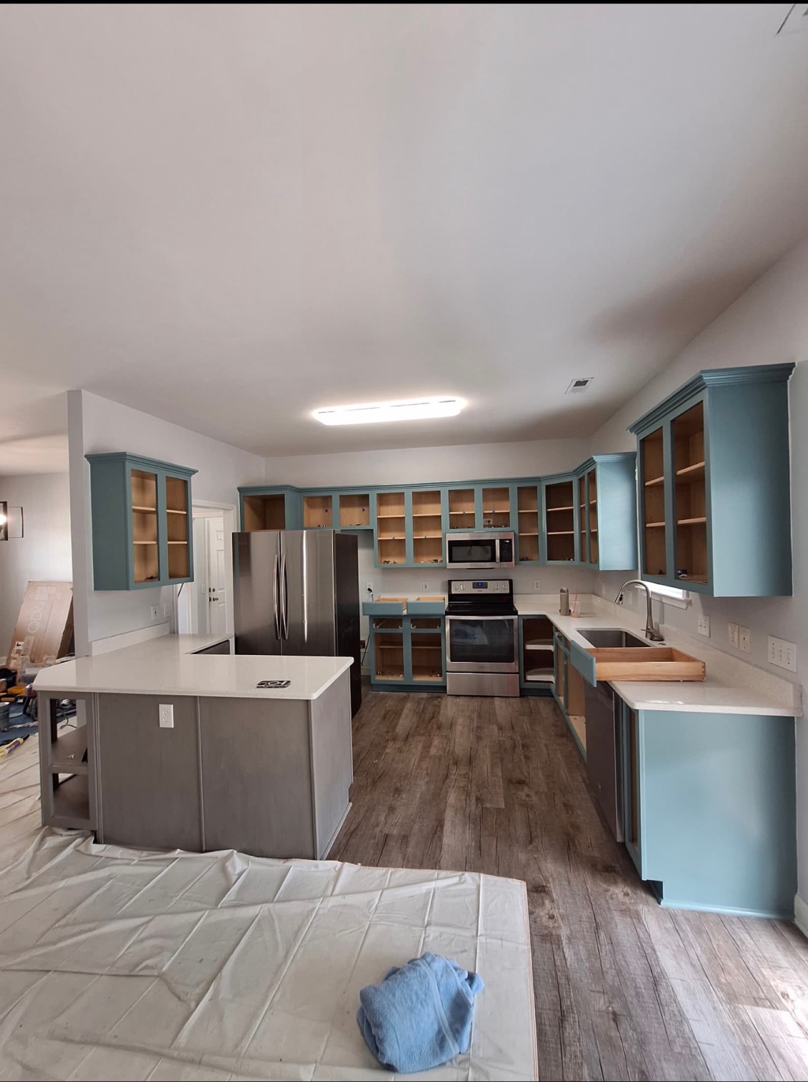 Kitchen mid-refinish with every cabinet door removed and drop cloths across the floor