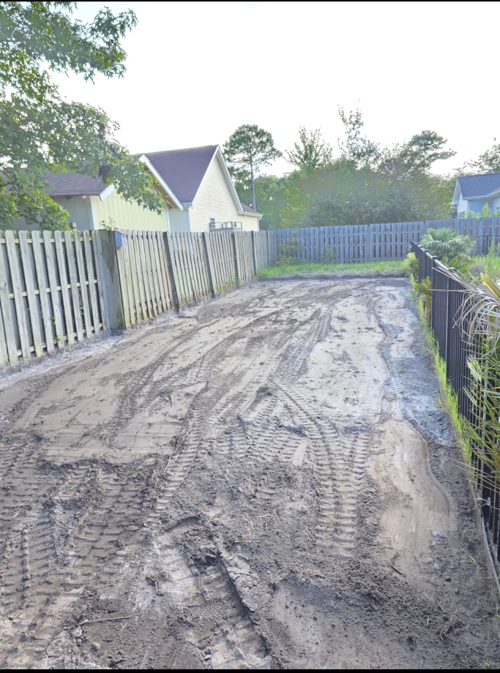 Bare rutted dirt side yard churned up by machine tracks